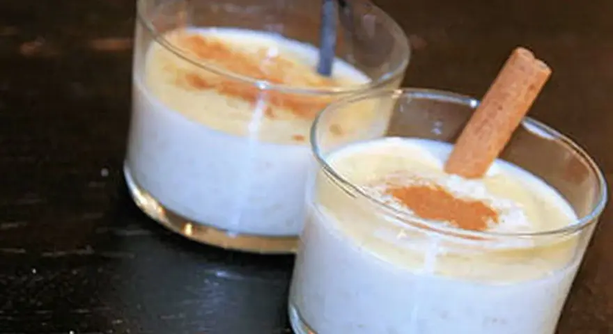 Deux verres de riz au lait crémeux, saupoudrés de cannelle. Un bâton de cannelle décore l'un des desserts, parfait pour une recette de riz au lait.