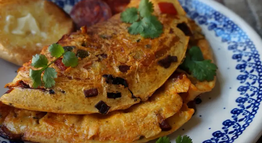 Pyszny omlet z chorizo, podany z grzankami i świeżą kolendrą, na talerzu z niebieskim wzorem.