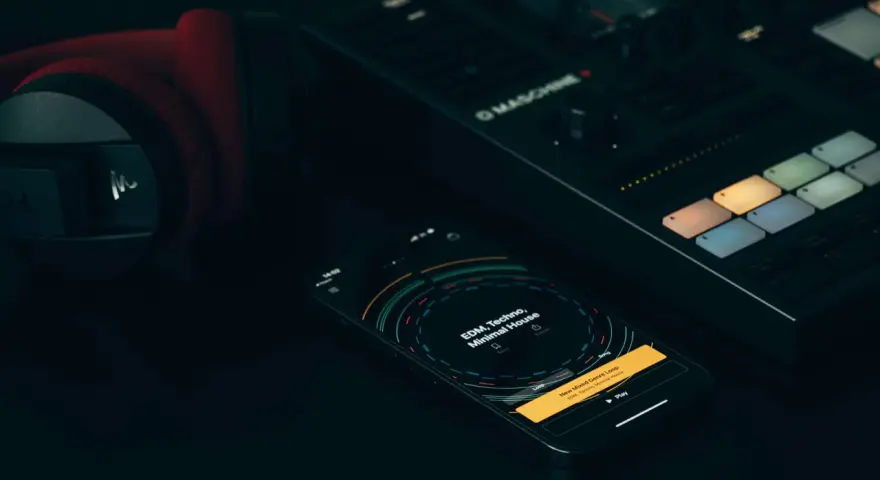 Czerwone słuchawki, kontroler Maschine i smartfon z aplikacją do tworzenia muzyki, gdzie widać koala sampler.
