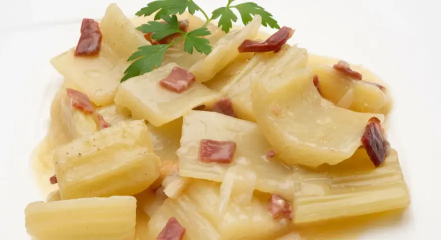 Cardo a la navarra, un plato tradicional con trozos tiernos de cardo en una cremosa salsa, adornado con trocitos de jamón y perejil fresco.