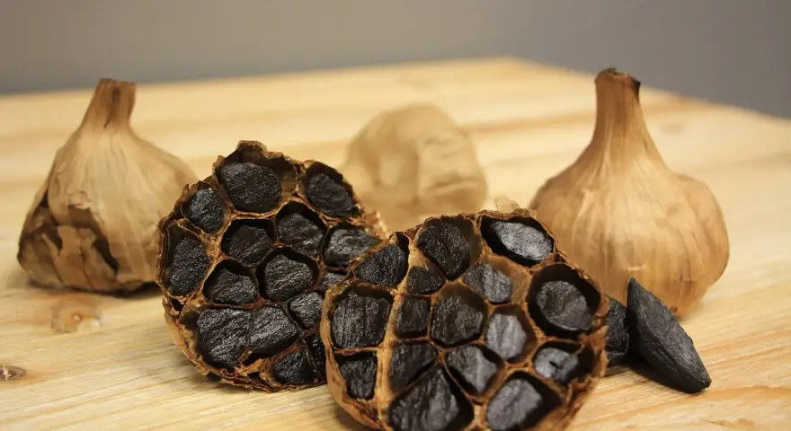 Ajos negros enteros y cortados, mostrando sus dientes oscuros y arrugados. Descubre las increíbles ajo negro propiedades.