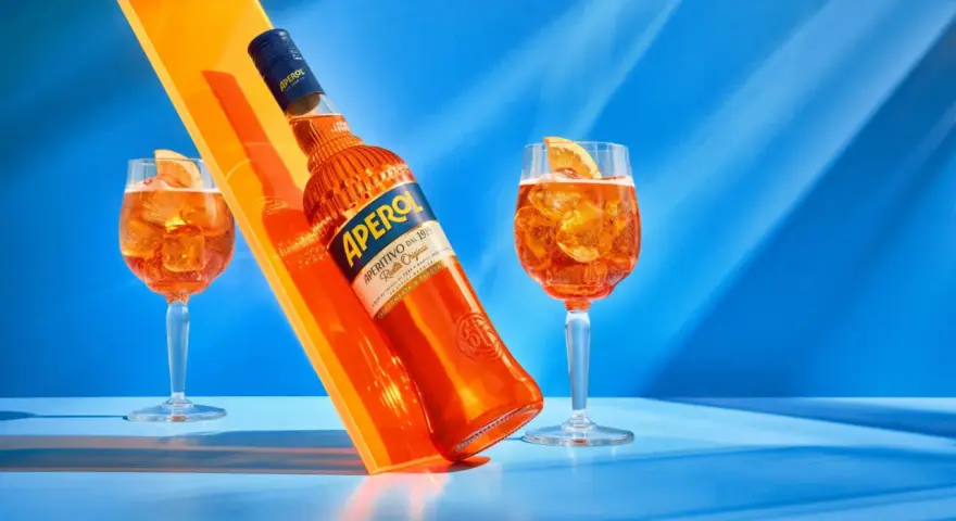 Aperol, znany z orzeźwiającego smaku, ma 11% alkoholu. Na zdjęciu butelka i dwa drinki z pomarańczą.