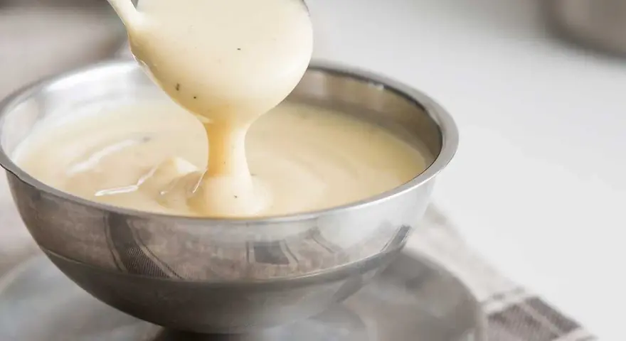 Krämig vaniljsås hälls upp ur en slev i en skål. Perfekt till efterrätt, här är ett enkelt vaniljsås recept.