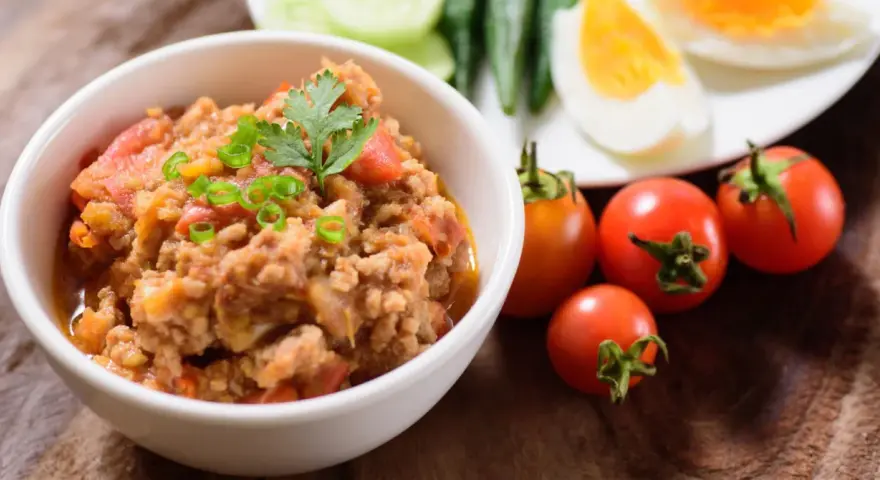 Pyszna pasta z makreli w pomidorach, udekorowana szczypiorkiem i natką. Obok świeże pomidorki i jajka na twardo.