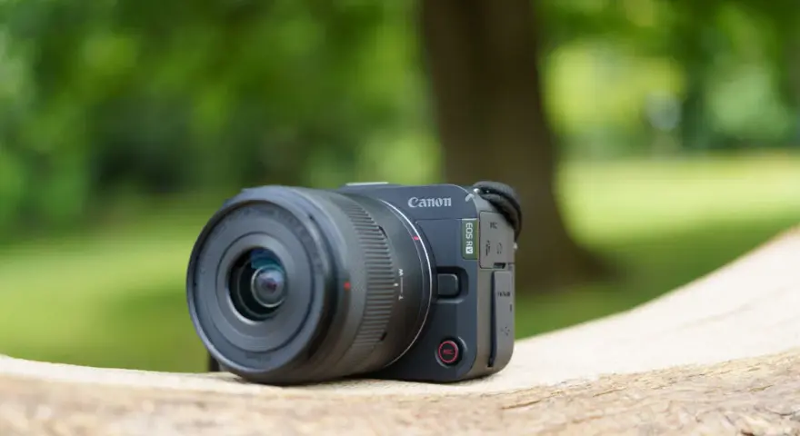 Un appareil photo Canon EOS R50, prêt pour un test en extérieur. Le soleil brille sur son objectif.