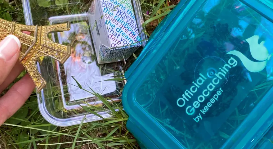 Złoty model Wieży Eiffla w pojemniku, obok niebieskiego pojemnika z napisem "Official Geocaching". To jest geocaching co to za zabawa!