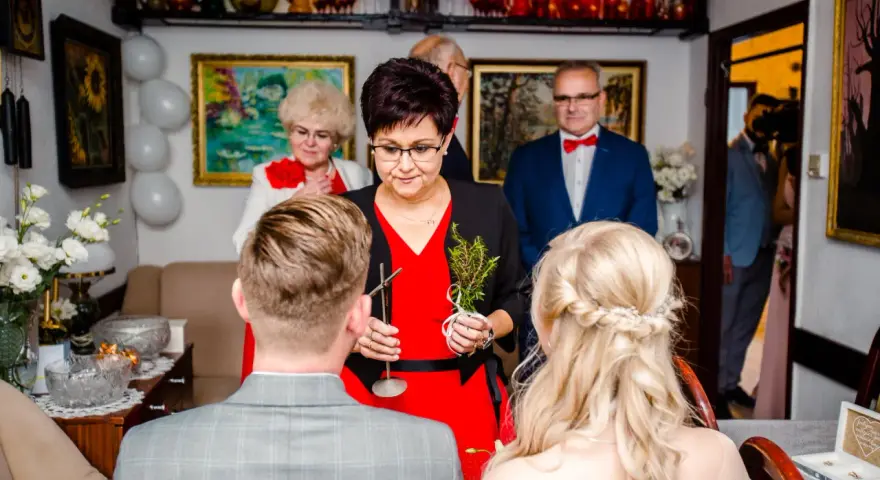 Tradycyjne błogosławieństwo pary młodej. Kobieta w czerwonej sukience trzyma gałązkę ziół, błogosławiąc narzeczonych.