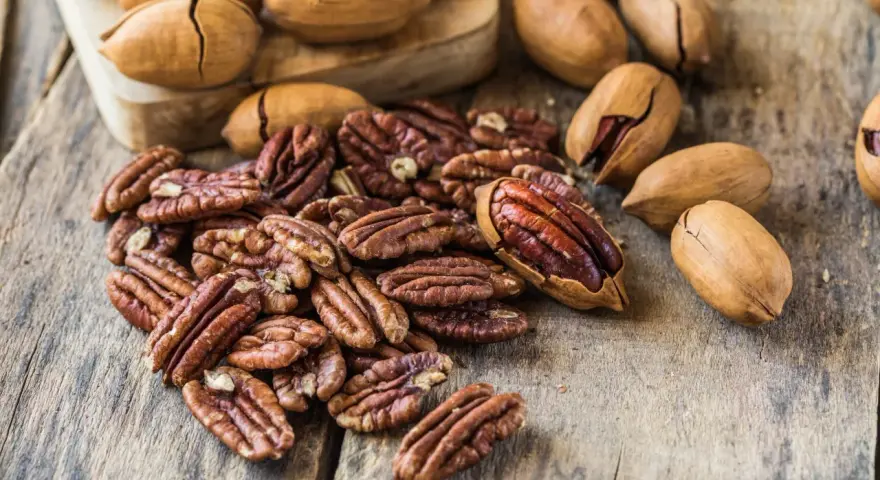 Noix de pécan décortiquées et entières sur fond de bois. Découvrez le noix de pécan bienfait pour une alimentation saine et gourmande.