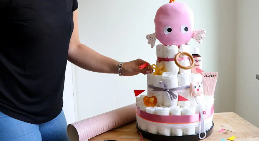 En person lägger sista handen vid en blöjtårta dekoration med en rosa bläckfisk som topp.