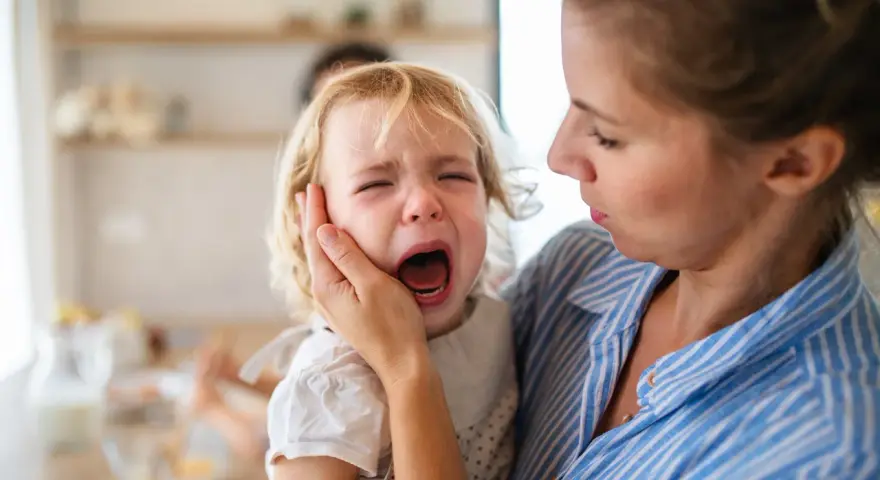 Mama próbuje uspokoić płaczące dziecko, które przeżywa histerię. 5-latek krzyczy, a mama delikatnie trzyma go za policzek.