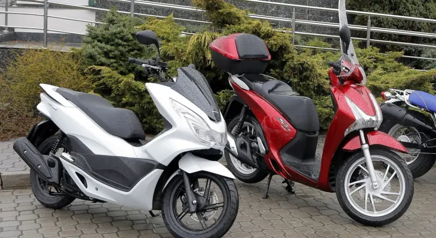 Biały i czerwony skuter stoją na mokrym bruku. Zastanawiasz się, ile oleju do skutera 4t?