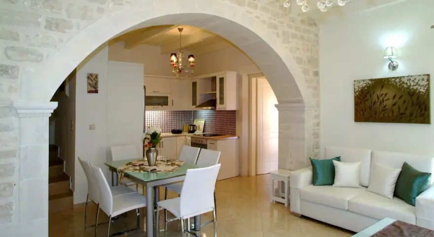 Un elegante soggiorno con un **arco in pietra moderno** che separa la zona pranzo dalla cucina. Divano bianco, quadri e lampadario di cristallo.