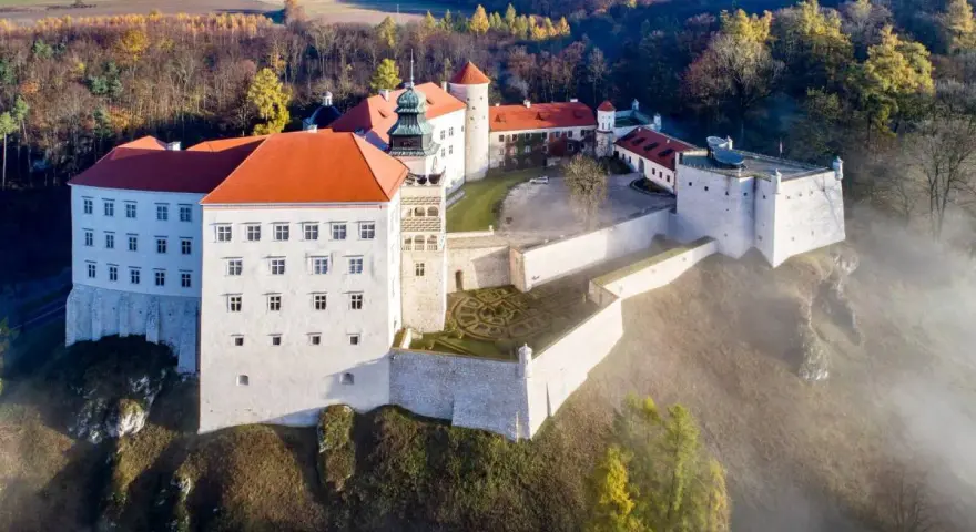 Majestatyczny zamek pod Krakowem, otoczony mgłą i jesiennym lasem, wznosi się na wzgórzu.