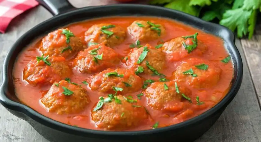Polpette di lenticchie in salsa di pomodoro, guarnite con prezzemolo fresco, servite in una padella nera su un tavolo di legno.