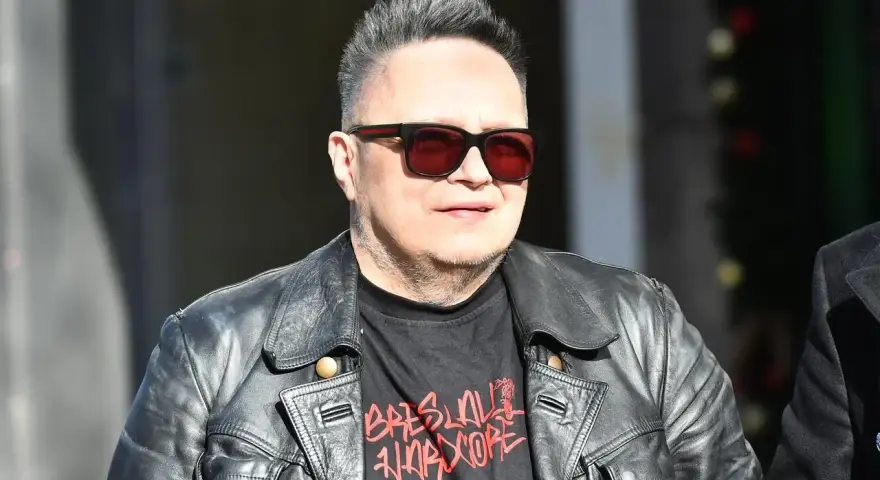 Charyzmatyczny wokalista w skórzanej kurtce i okularach przeciwsłonecznych, z charakterystyczną fryzurą.