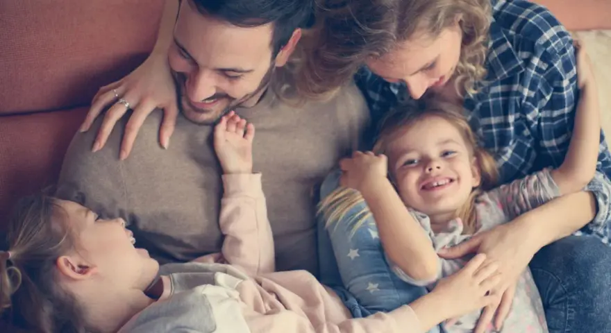 Glückliche Familie kuschelt auf dem Sofa. Zwei Elternteile umarmen ihre zwei Kinder, die sich an sie schmiegen.