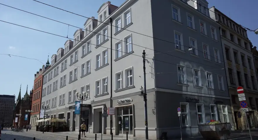 Elegancki hotel Korona Wrocław z szarym frontem i białymi oknami, na tle błękitnego nieba.