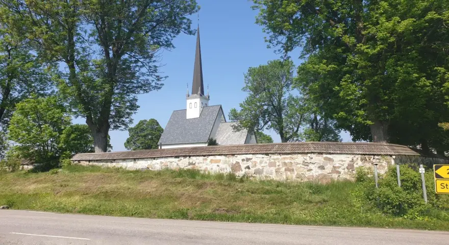 Kyrka med spira bakom stenmur och träd. En skylt visar "2 St". Kanske en vy från Hamar, Norge.