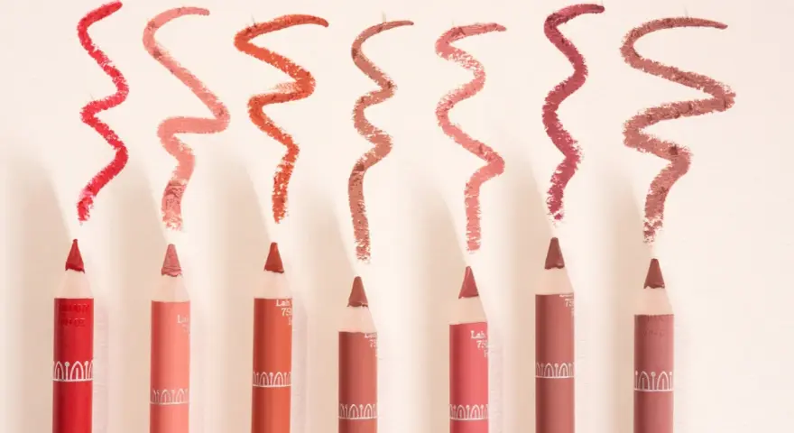 Plusieurs crayons à lèvres de différentes teintes, avec des échantillons de leur utilisation en traits ondulés.