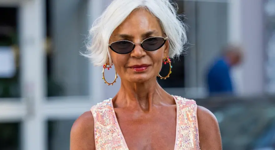 Frau mit weißem Kurzhaarschnitt, Sonnenbrille und auffälligem Schmuck.