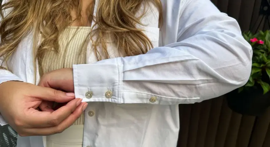 Sotto una camicia bianca, un top a coste color crema. Dettagli sui polsini con gemelli.