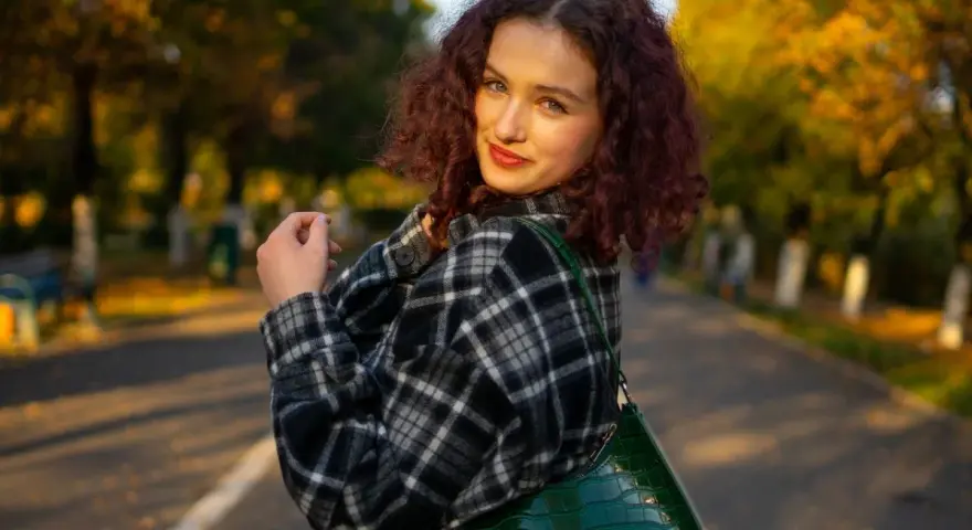 Dziewczyna w kratę, co to za styl? Ciepła flanela i zielona torebka na tle jesiennego parku.