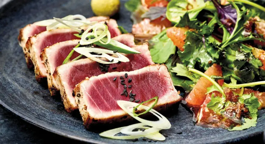 Tataki de atún perfectamente sellado, servido con una ensalada fresca de cítricos y hojas verdes.