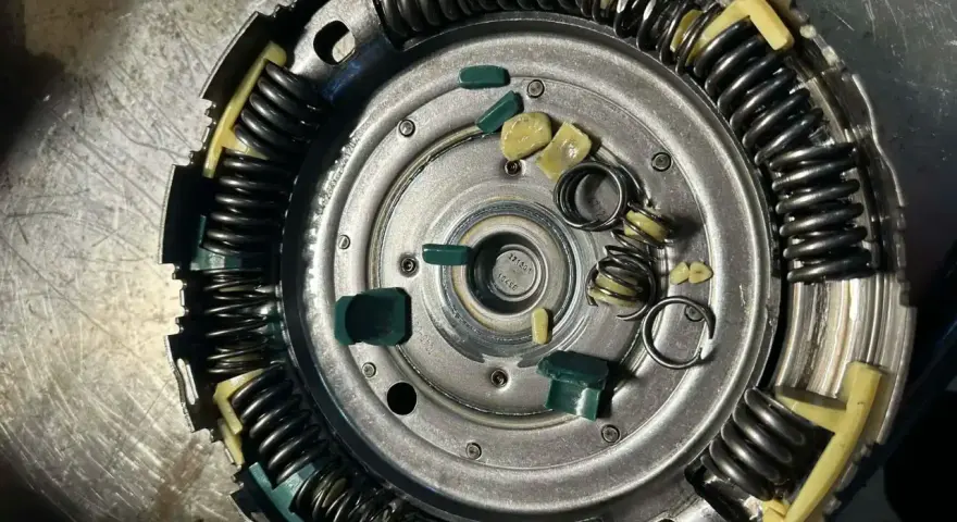 Zużyte elementy sprzęgła powershift: połamane zielone wkładki i sprężyny, objawy zużycia widoczne na metalowych częściach.