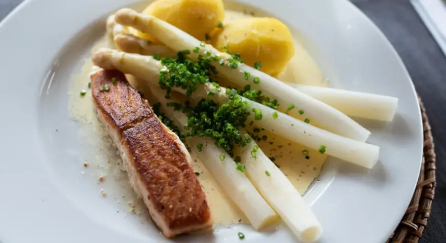 Ein Stück Lachs mit Spargel, Kartoffeln und Sauce Hollandaise. Der Spargel ist mit Schnittlauch bestreut.