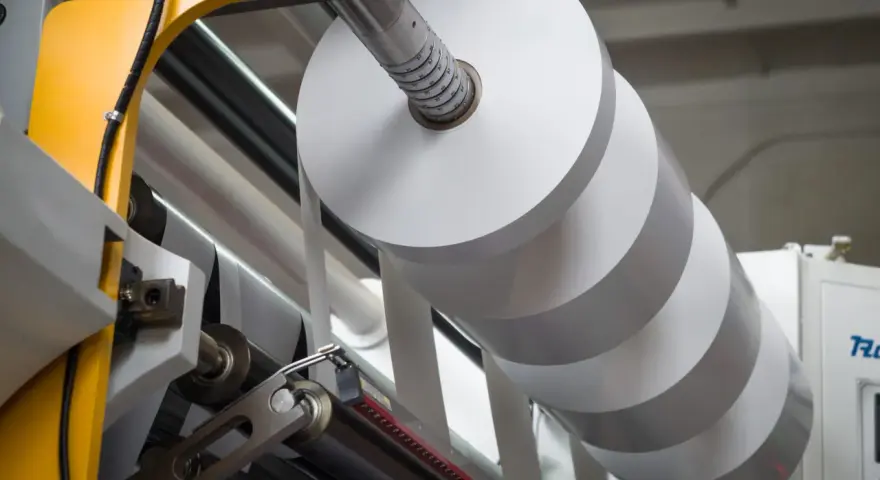 Rollo gigante de papel blanco en una máquina industrial. La densidad del papel es clave para la calidad de impresión.