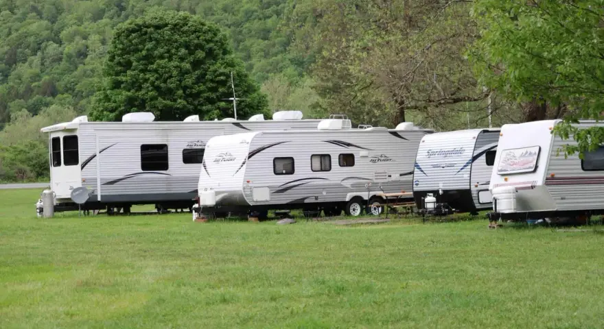 Rząd przyczep kempingowych na zielonej trawie, w tle las. Idealne miejsce na camping Górna Wetlinka.