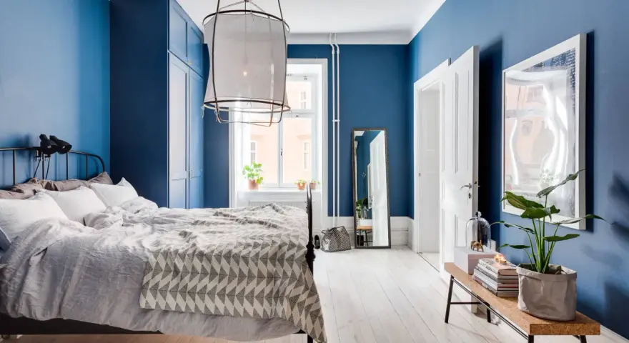 Accogliente camera da letto blu con letto comodo, armadio scuro e specchio a figura intera.