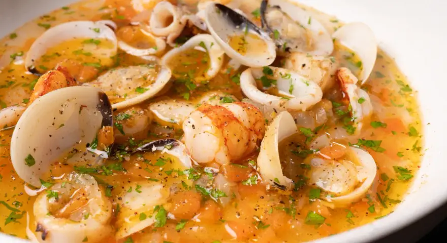 Sopa de mariscos con gambas, calamares y almejas en un caldo dorado con perejil.