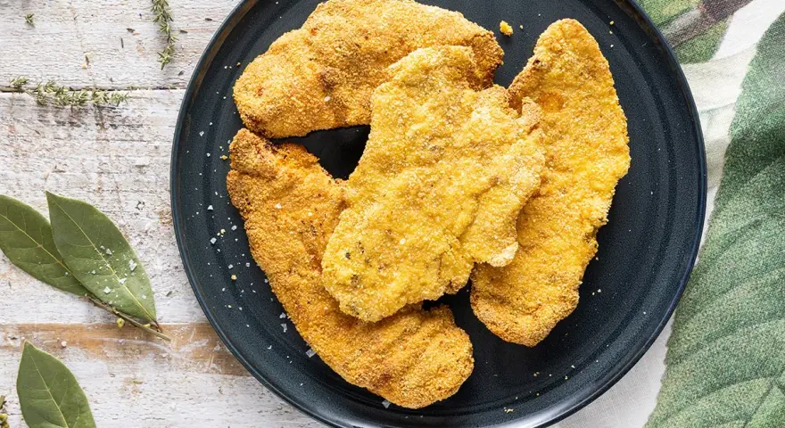 Cotolette dorate e croccanti, perfette cotolette in friggitrice ad aria, servite su un piatto scuro con erbe aromatiche e foglie di alloro.