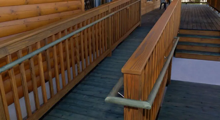 A wooden wheelchair ramp with railings curves around a log cabin. This shows how to build a wheelchair ramp for accessibility.