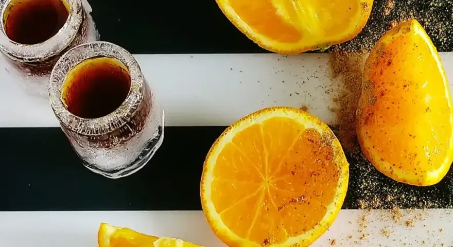 Dwa kieliszki z Jägermeisterem ze spritem, obok pokrojone pomarańcze posypane przyprawami.