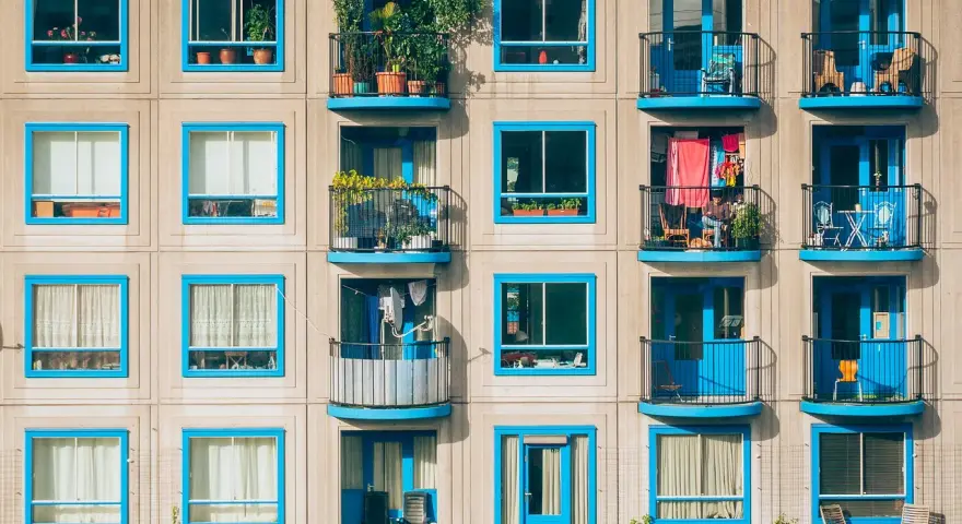 Elegancka loggia i balkon z niebieskimi ramami okiennymi, pełne zieleni i suszącego się prania, tworzą kolorowy kontrast na betonowej fasadzie.