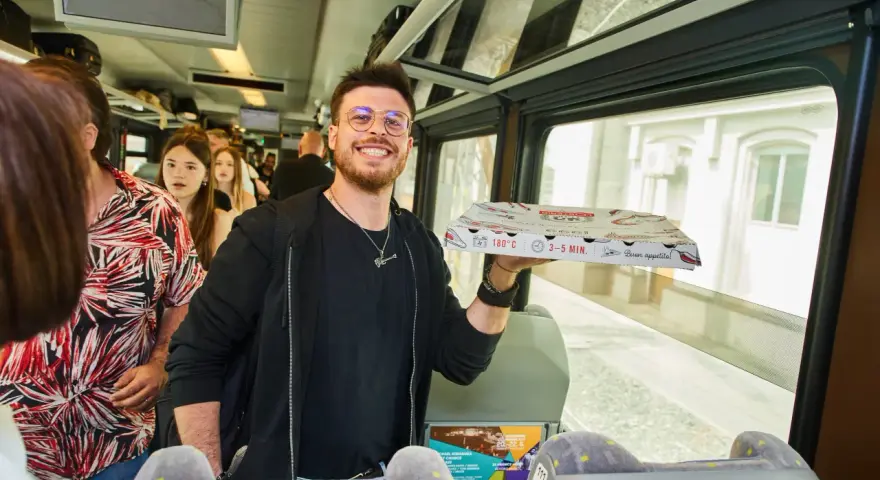 Uśmiechnięty mężczyzna z pizzą w ręku w pociągu relacji Kraków-Praga.
