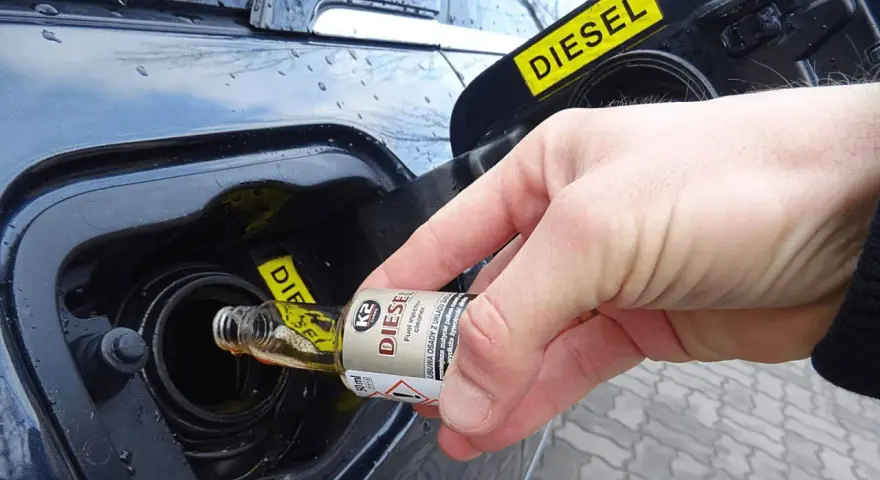 Dłoń wlewa dodatek do benzyny do baku samochodu z napisem DIESEL.