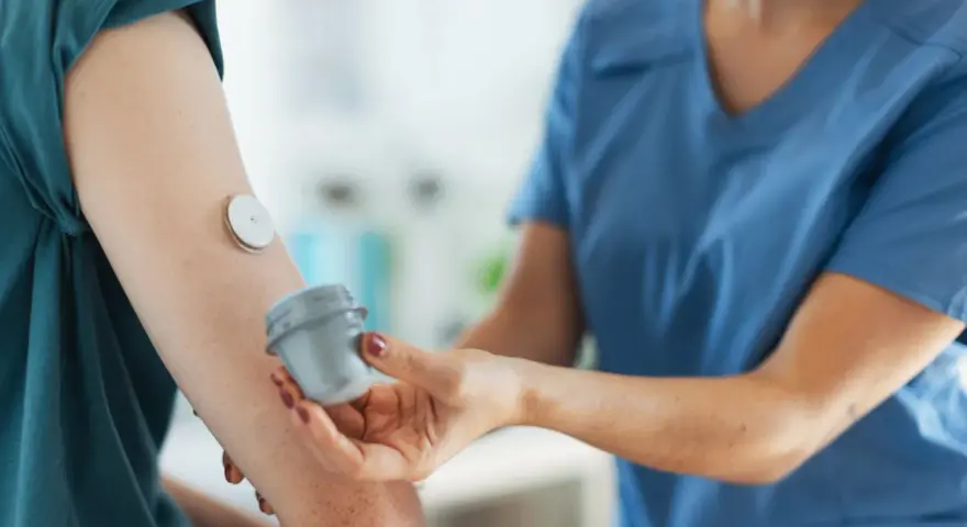 Lekarz od chorób metabolicznych pomaga pacjentowi z glukometrem na ramieniu.