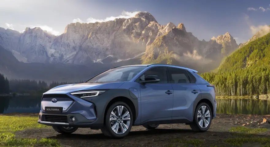 Niebieski Subaru Solterra stoi nad jeziorem z górami w tle.
