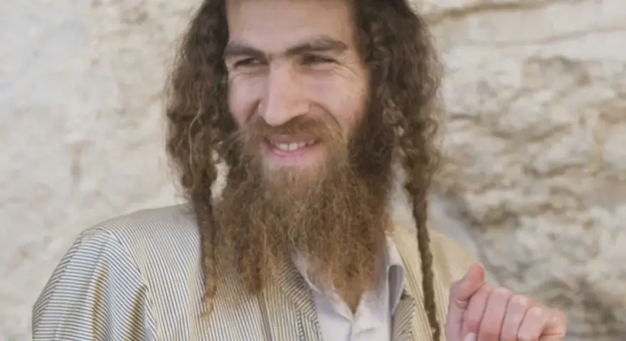 A smiling man with long, curly hair and a beard, wearing traditional Jewish attire. His appearance sparks curiosity about what ethnicity was Jesus.