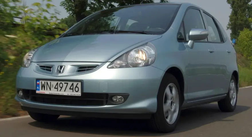 Jasnoniebieski Honda Jazz 2 na drodze, z zielenią w tle.