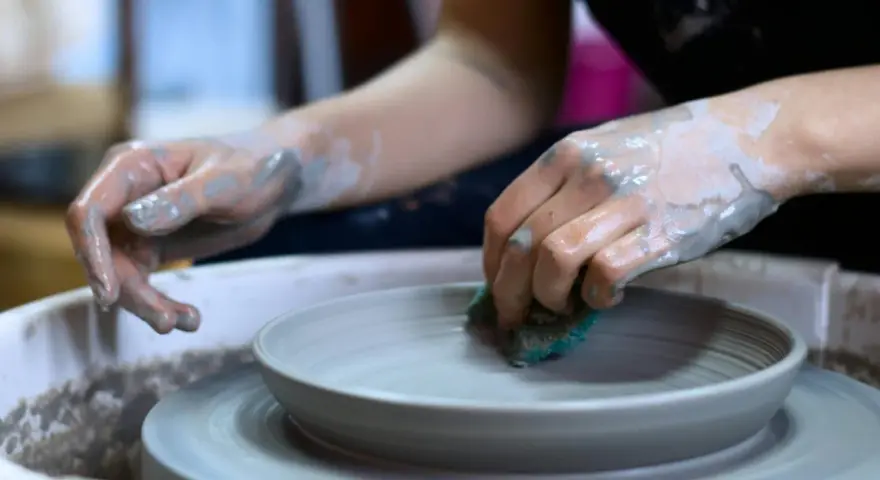 Mani sporche di argilla lavorano su un piatto al tornio, creando forme uniche con lavori con argilla senza cottura.