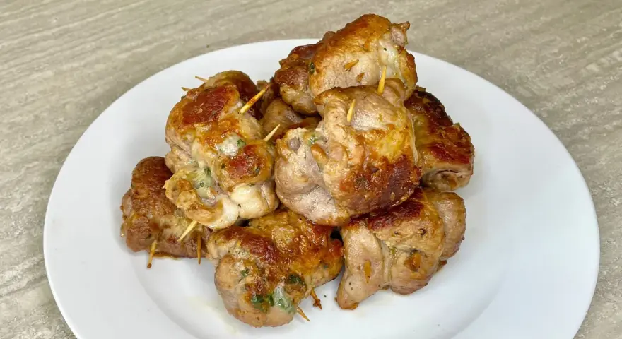 Un mucchio di bombette pugliesi ricetta, dorate e succulente, tenute insieme da stuzzicadenti, su un piatto bianco.