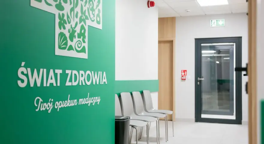 Zielona ściana z napisem "Świat Zdrowia", rząd krzeseł i drzwi w poczekalni kliniki.