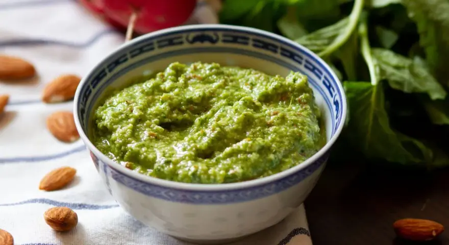 Zielone pesto z liści rzodkiewki, z migdałami i świeżymi liśćmi w tle. Idealne do makaronu lub jako dodatek do kanapek.