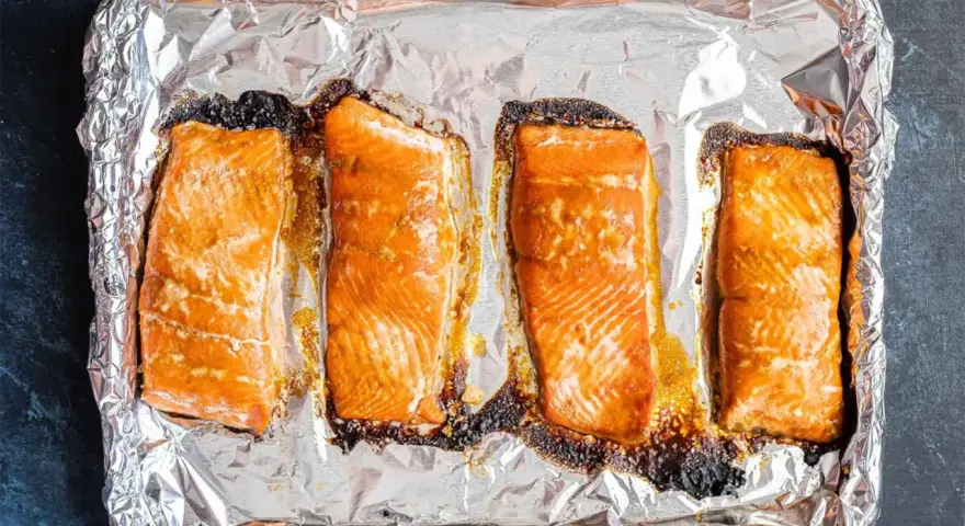 Cztery kawałki pieczonego łososia na folii aluminiowej. Idealny łosoś do sushi, lekko przypieczony na brzegach, zachęca do przygotowania.