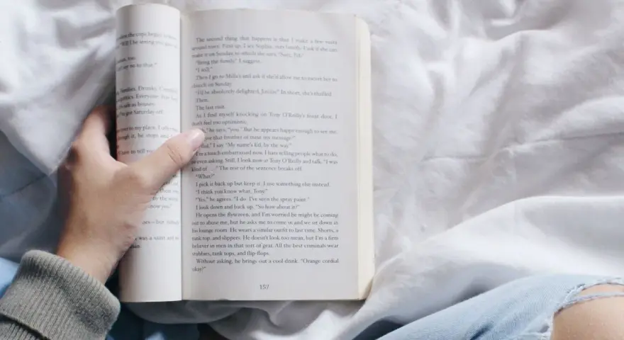 Mano sosteniendo un libro abierto con relatos cortos para mujeres. La página muestra texto y el número 157.