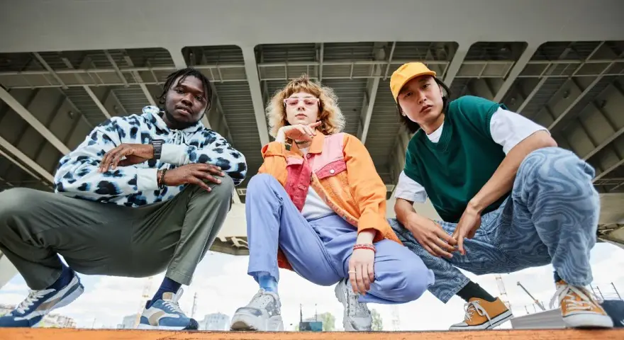 Tre giovani con look urbani, ognuno con le sue sneakers, mostrano cosa sono le sneakers: calzature comode e alla moda per ogni stile.